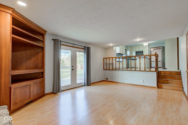 unfurnished living room with stairway, visible vents, baseboards, and light wood-style floors