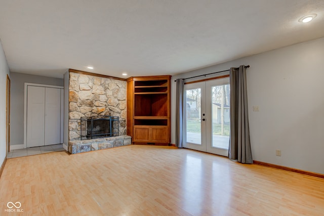 unfurnished living room with french doors, baseboards, a fireplace, and light wood finished floors