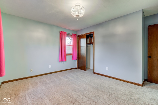 unfurnished bedroom featuring a closet, a notable chandelier, baseboards, and carpet floors