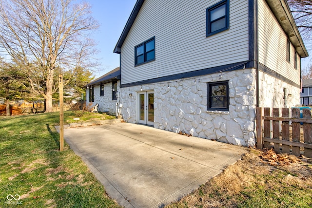 view of side of property featuring stone siding, fence, french doors, a yard, and a patio area