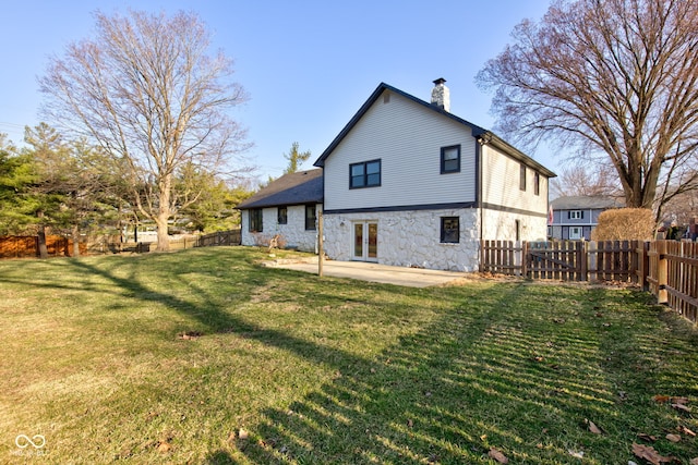 rear view of house with french doors, stone siding, a fenced backyard, and a chimney