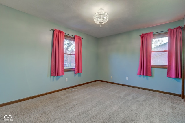 carpeted spare room featuring a chandelier, visible vents, baseboards, and a wealth of natural light