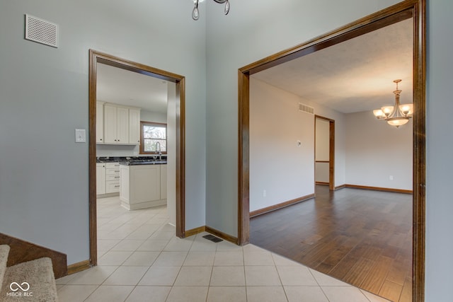 hall with light tile patterned floors, visible vents, baseboards, and a chandelier