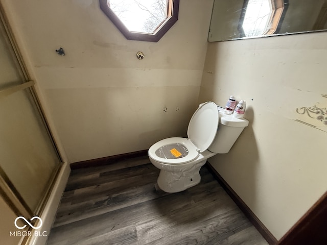 bathroom with toilet, wood finished floors, baseboards, and a shower with door