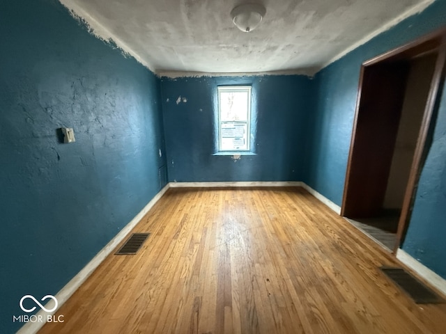 empty room featuring hardwood / wood-style floors, baseboards, and visible vents