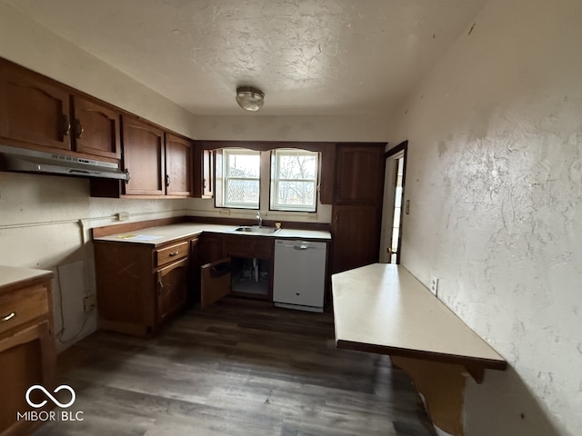 kitchen with a sink, under cabinet range hood, dishwasher, a textured wall, and dark wood-style flooring