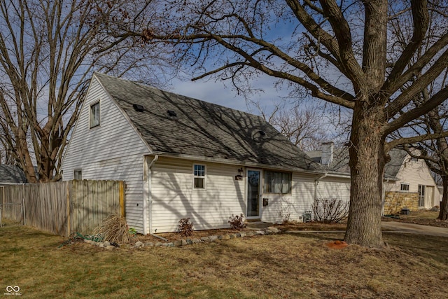 view of side of property featuring a lawn, a chimney, roof with shingles, and fence