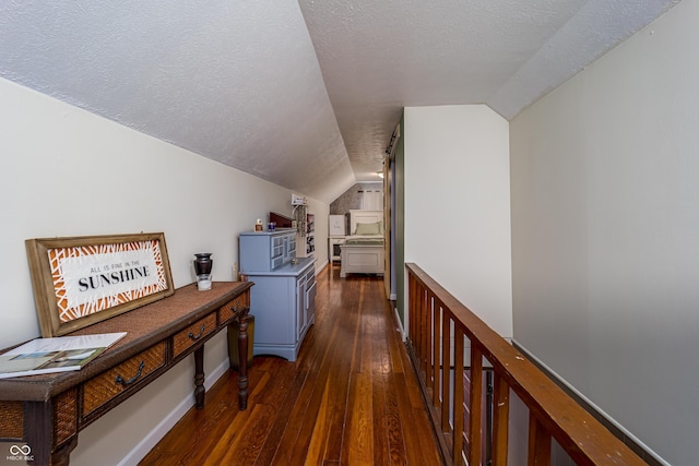 hall with a textured ceiling, dark wood-style floors, and vaulted ceiling