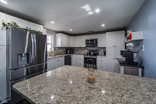 kitchen featuring light stone countertops, decorative backsplash, appliances with stainless steel finishes, white cabinets, and a sink