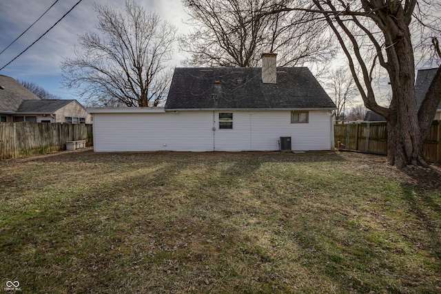 rear view of house with cooling unit, roof with shingles, a fenced backyard, a chimney, and a lawn