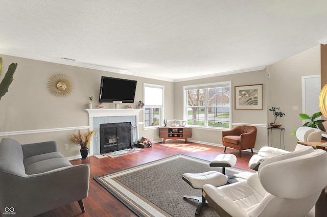 living area featuring a fireplace with flush hearth, visible vents, ornamental molding, and wood finished floors