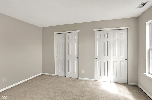 unfurnished bedroom featuring carpet flooring, visible vents, baseboards, and multiple closets