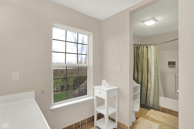 bathroom with a wealth of natural light, tile patterned flooring, baseboards, and toilet