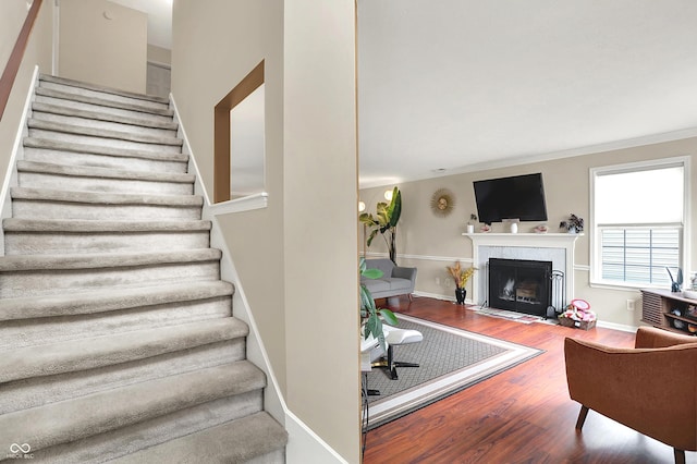 stairs with a fireplace with flush hearth, baseboards, crown molding, and wood finished floors