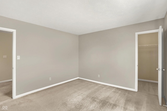 unfurnished bedroom with a closet, a walk in closet, carpet, and baseboards
