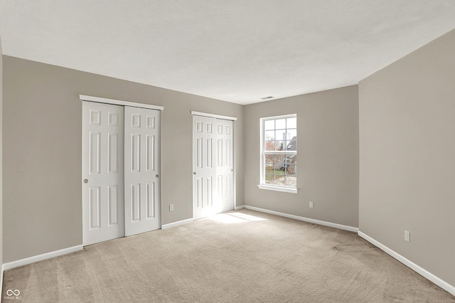 unfurnished bedroom featuring baseboards, carpet flooring, and two closets
