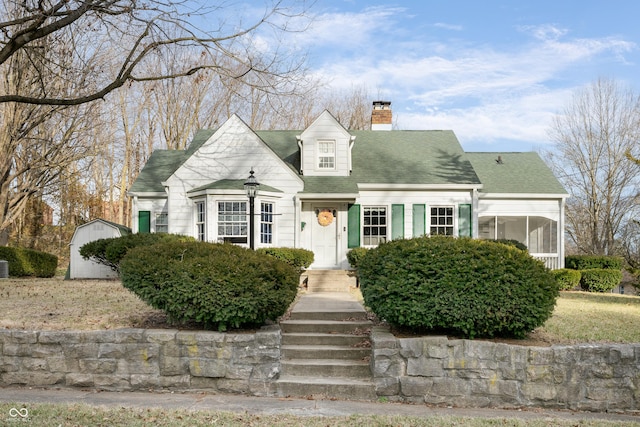 cape cod home with roof with shingles, a sunroom, and a chimney