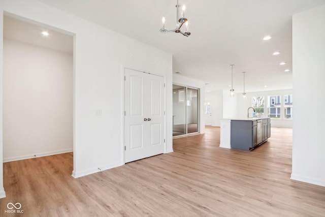 unfurnished living room with light wood finished floors, baseboards, recessed lighting, a notable chandelier, and a sink