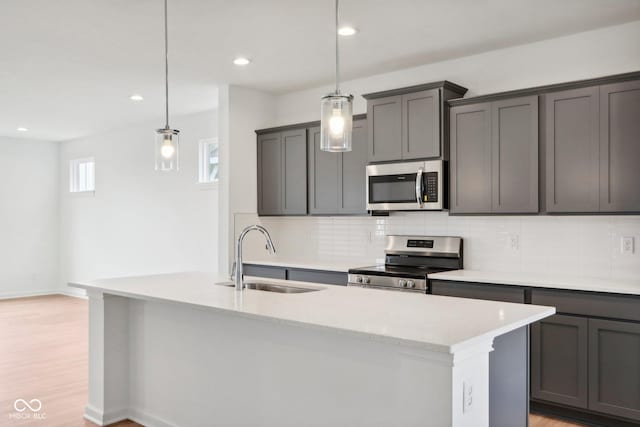 kitchen featuring light wood finished floors, decorative backsplash, appliances with stainless steel finishes, and a sink