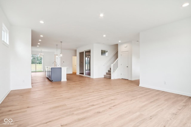 unfurnished living room with an inviting chandelier, stairway, recessed lighting, and light wood-style flooring