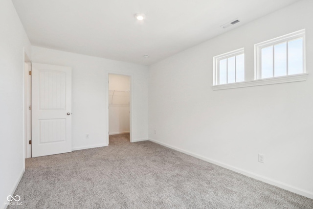 unfurnished bedroom featuring visible vents, a walk in closet, baseboards, carpet floors, and a closet