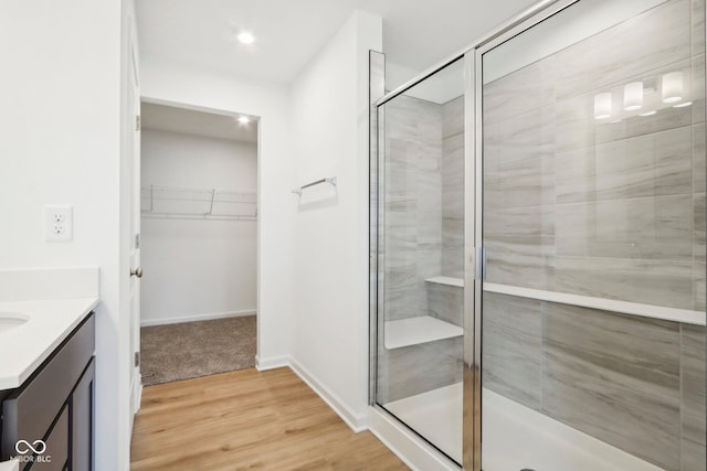 full bath featuring vanity, a spacious closet, wood finished floors, and a stall shower