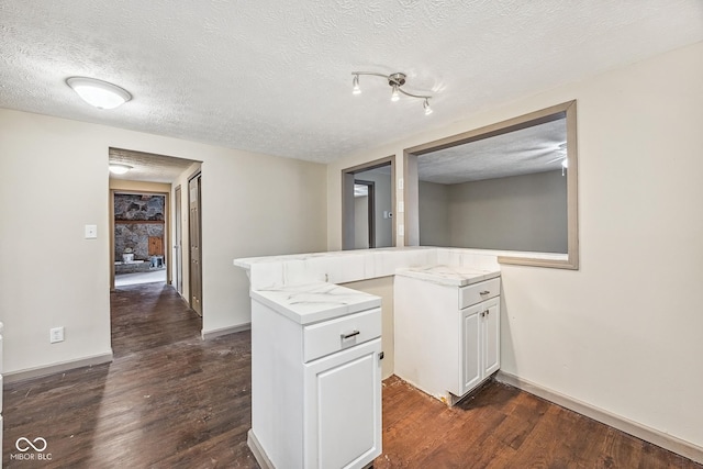 kitchen with white cabinets, a peninsula, a textured ceiling, and dark wood-type flooring