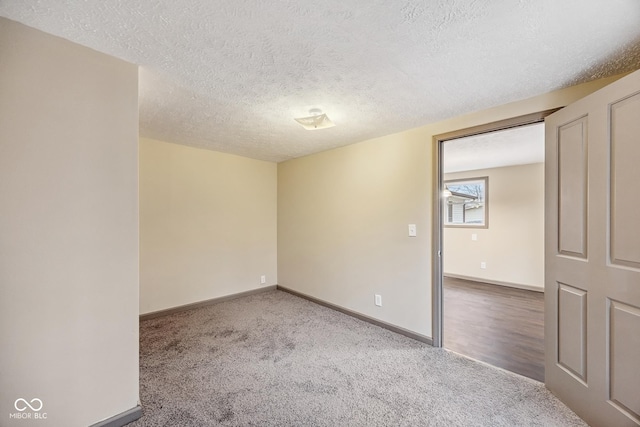 carpeted spare room featuring a textured ceiling and baseboards