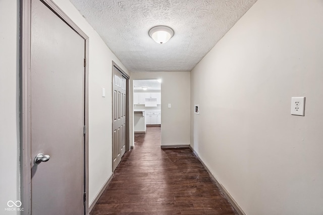 hallway featuring a textured ceiling, baseboards, and dark wood-style flooring