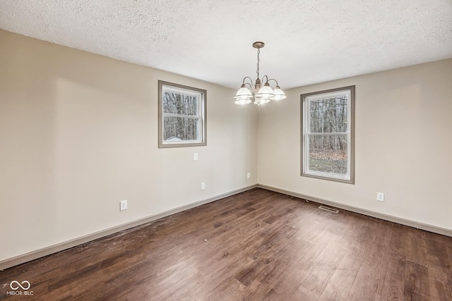 unfurnished room with visible vents, baseboards, an inviting chandelier, wood finished floors, and a textured ceiling