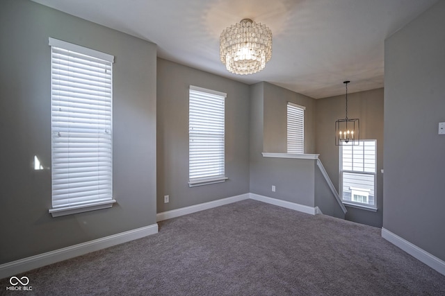 carpeted spare room featuring a notable chandelier and baseboards