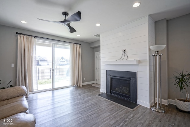 living area featuring a glass covered fireplace, visible vents, baseboards, and wood finished floors