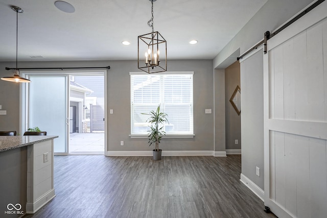 unfurnished dining area featuring visible vents, baseboards, dark wood-type flooring, a barn door, and a notable chandelier