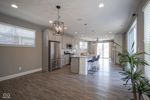 kitchen featuring dark wood-type flooring, baseboards, a breakfast bar area, stainless steel appliances, and a kitchen island with sink