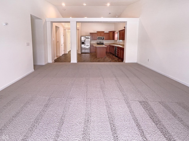 unfurnished living room with carpet flooring, a sink, baseboards, and vaulted ceiling