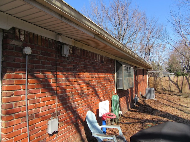 view of side of home with brick siding, central AC unit, and fence