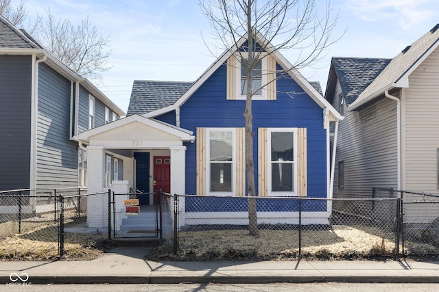 view of front of property with a fenced front yard, roof with shingles, and a gate