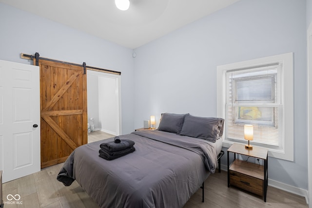 bedroom featuring a barn door, baseboards, and light wood-type flooring