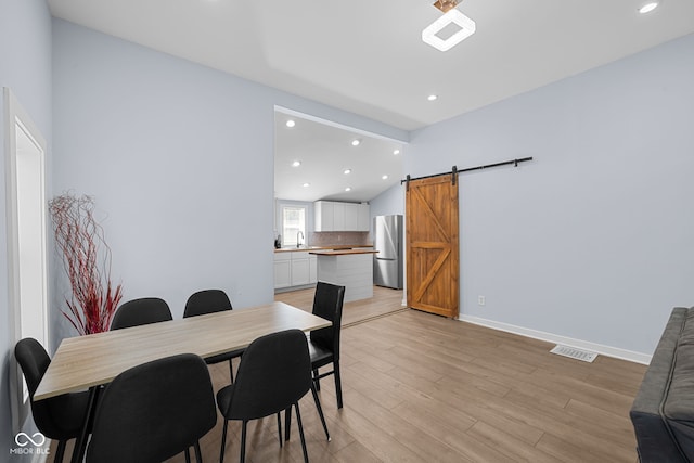 dining area featuring visible vents, baseboards, lofted ceiling, light wood-style floors, and a barn door