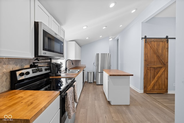 kitchen with a sink, appliances with stainless steel finishes, a barn door, backsplash, and butcher block counters