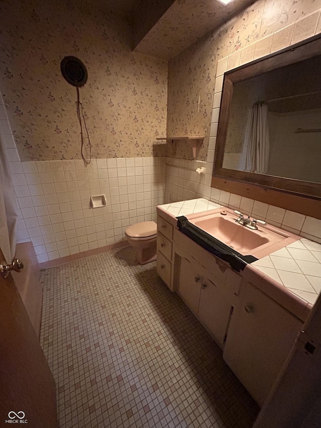 bathroom with a shower with shower curtain, a wainscoted wall, wallpapered walls, tile patterned flooring, and toilet