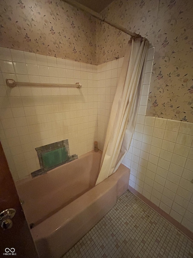 bathroom featuring wallpapered walls, a wainscoted wall, tile patterned floors, tile walls, and shower / bathtub combination with curtain