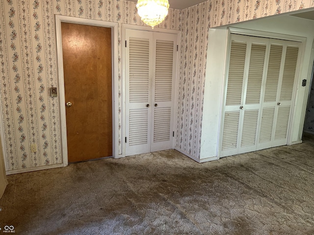 unfurnished bedroom featuring a notable chandelier, two closets, wallpapered walls, and carpet floors