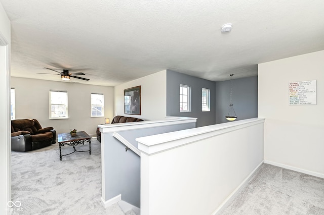 hallway with baseboards, an upstairs landing, carpet, and a textured ceiling