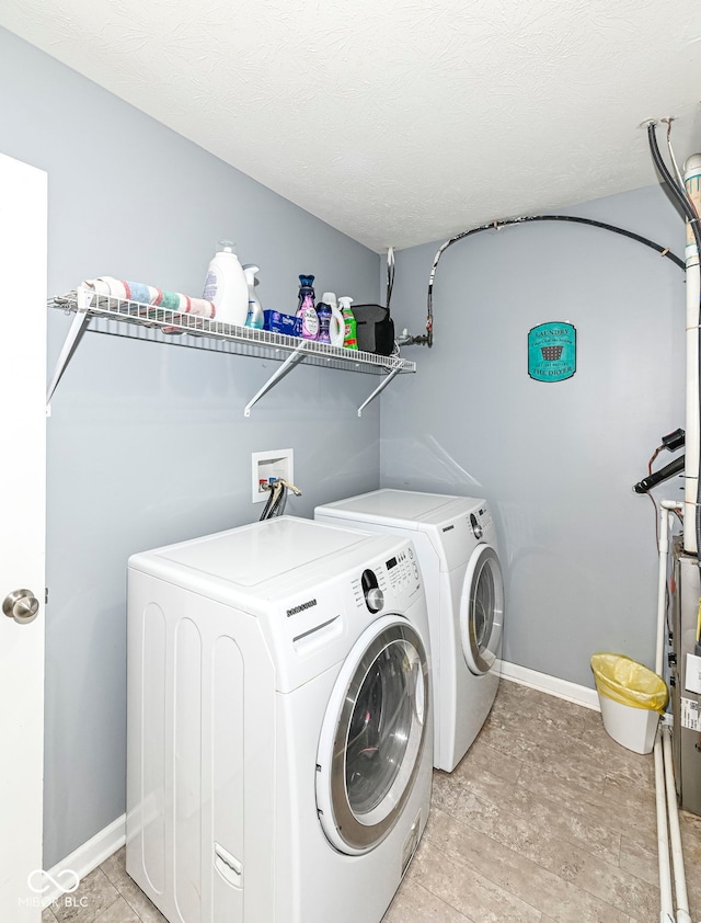 clothes washing area featuring washer and clothes dryer, laundry area, a textured ceiling, and baseboards