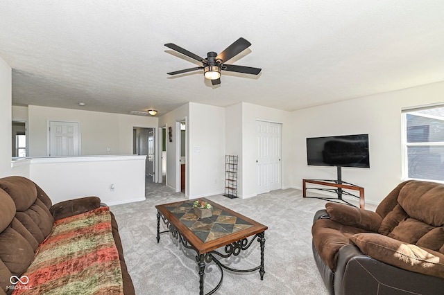 living area featuring baseboards, light carpet, a textured ceiling, and ceiling fan