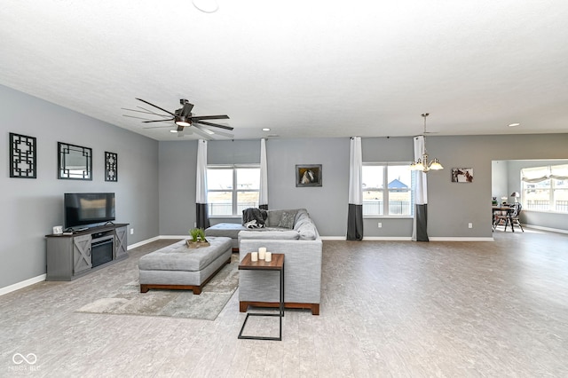 living room featuring a healthy amount of sunlight, ceiling fan with notable chandelier, and baseboards