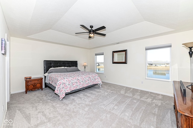 bedroom featuring ceiling fan, a raised ceiling, baseboards, and light carpet