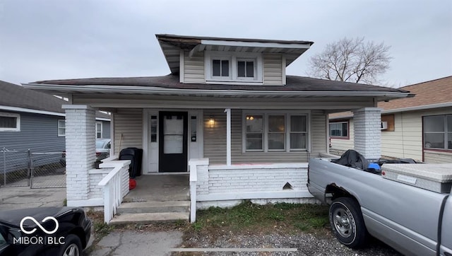 bungalow-style home featuring brick siding, a porch, and fence