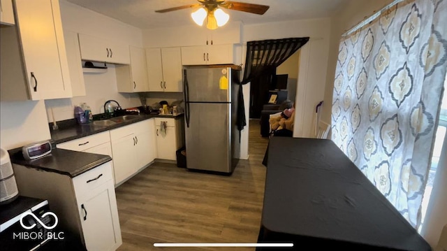 kitchen with dark wood-type flooring, a sink, dark countertops, freestanding refrigerator, and white cabinets